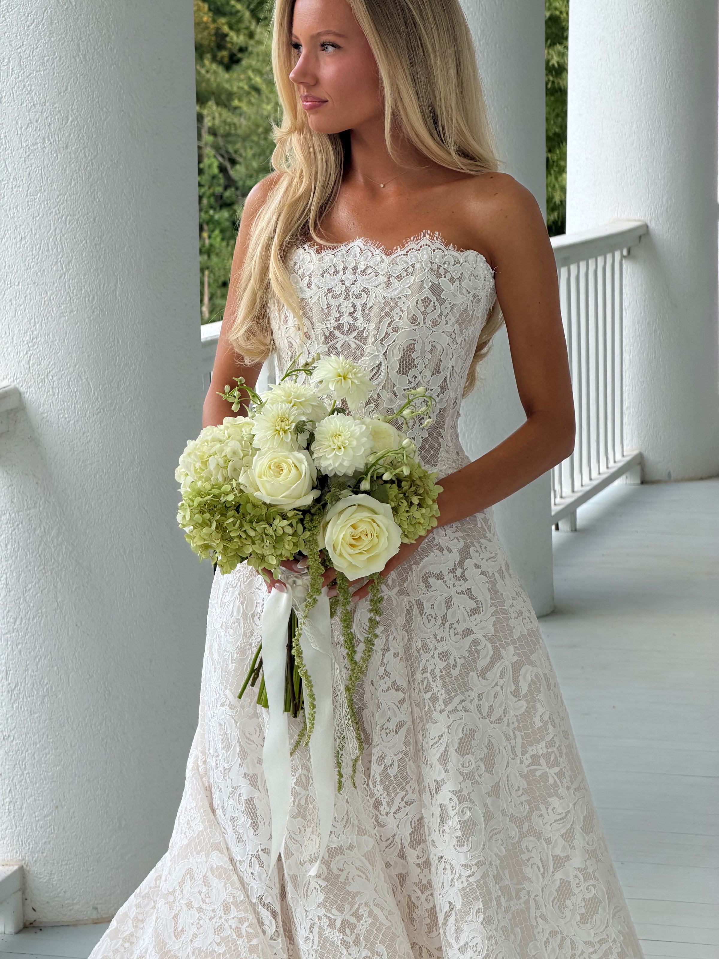Bride in a strapless lace gown holding white roses and green hydrangeas on a white columned porch