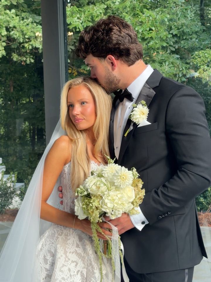 Groom leaning in to kiss the bride as she holds a white rose bouquet