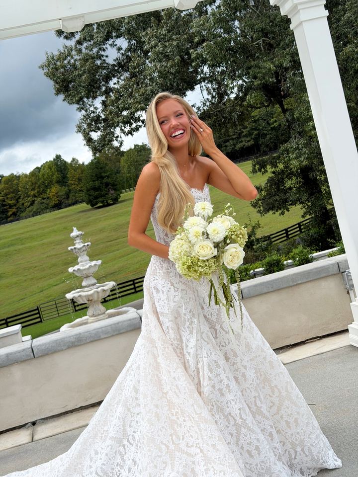 Bride laughing in a lace dress, holding a white rose bouquet on a porch